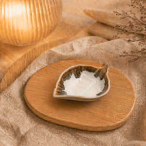 Witbruin keramisch schaaltje in bladvorm op houten plateau in warme sfeersetting met lamp en beige stof.