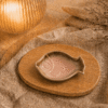 Roze keramisch visschaaltje op houten plateau in warme sfeersetting met lamp en decoratieve takjes.