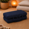 Donkerblauw draagbaar meditatiekussen ingeklapt op een naturel vloerkleed in een warme meditatiehoek.
