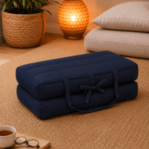 Donkerblauw draagbaar meditatiekussen ingeklapt op een naturel vloerkleed in een warme meditatiehoek.