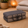 Draagbaar meditatiekussen in grijs en beige op een naturel vloerkleed in een warme meditatiehoek met sfeerlamp.