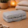 Grijs draagbaar meditatiekussen ingeklapt op een naturel vloerkleed in een warme meditatiehoek.