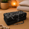 Draagbaar meditatiekussen in zwart met witte print op een naturel vloerkleed in een warme meditatiehoek.