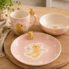 Sfeervolle foto van roze Kinderservies Teddy met mok, kom en bord op houten tafel met lieve berenfiguurtjes.
