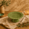 Groene keramische presenteerschaal van 18 cm op voet met bloemreliëf in een warme natuurlijke tafelsetting.