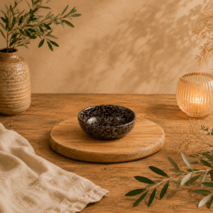 Zwart-bruin gespikkeld keramisch schaaltje van 8,5 cm op een houten serveerplank in een warme natuurlijke setting.