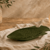 Groen keramisch visbord in visvorm op een houten tafel met warme natuurlijke sfeerdecoratie.