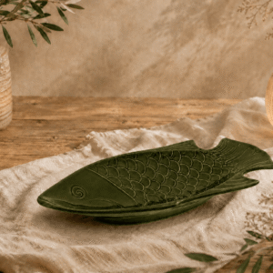 Groen keramisch visbord in visvorm op een houten tafel met warme natuurlijke sfeerdecoratie.