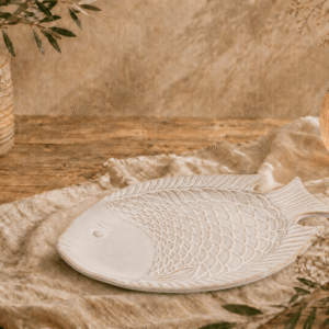 Wit-bruin keramisch visbord in visvorm op een houten tafel met warme natuurlijke sfeerdecoratie.