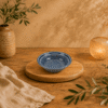 Handgemaakt keramisch rond Lanna schaaltje met visreliëf in blauw op houten tafel in warme sfeervolle setting