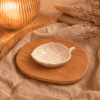 Wit gespikkeld keramisch bladschaaltje van 12,5 cm, sfeervol gepresenteerd op een houten schaal met beige textiel en warme verlichting.