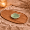 groen keramisch bladschaaltje van 10 cm, sfeervol gepresenteerd op een houten schaal met beige textiel en warme verlichting.