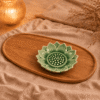 Lichtgroen keramieken lotusschaaltje van 10 cm met bloemvormig reliëf op een ovaal houten dienblad, sfeervol gestyled met beige linnen en kaarslicht.