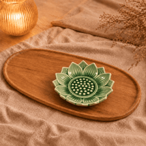 Lichtgroen keramieken lotusschaaltje van 10 cm met bloemvormig reliëf op een ovaal houten dienblad, sfeervol gestyled met beige linnen en kaarslicht.