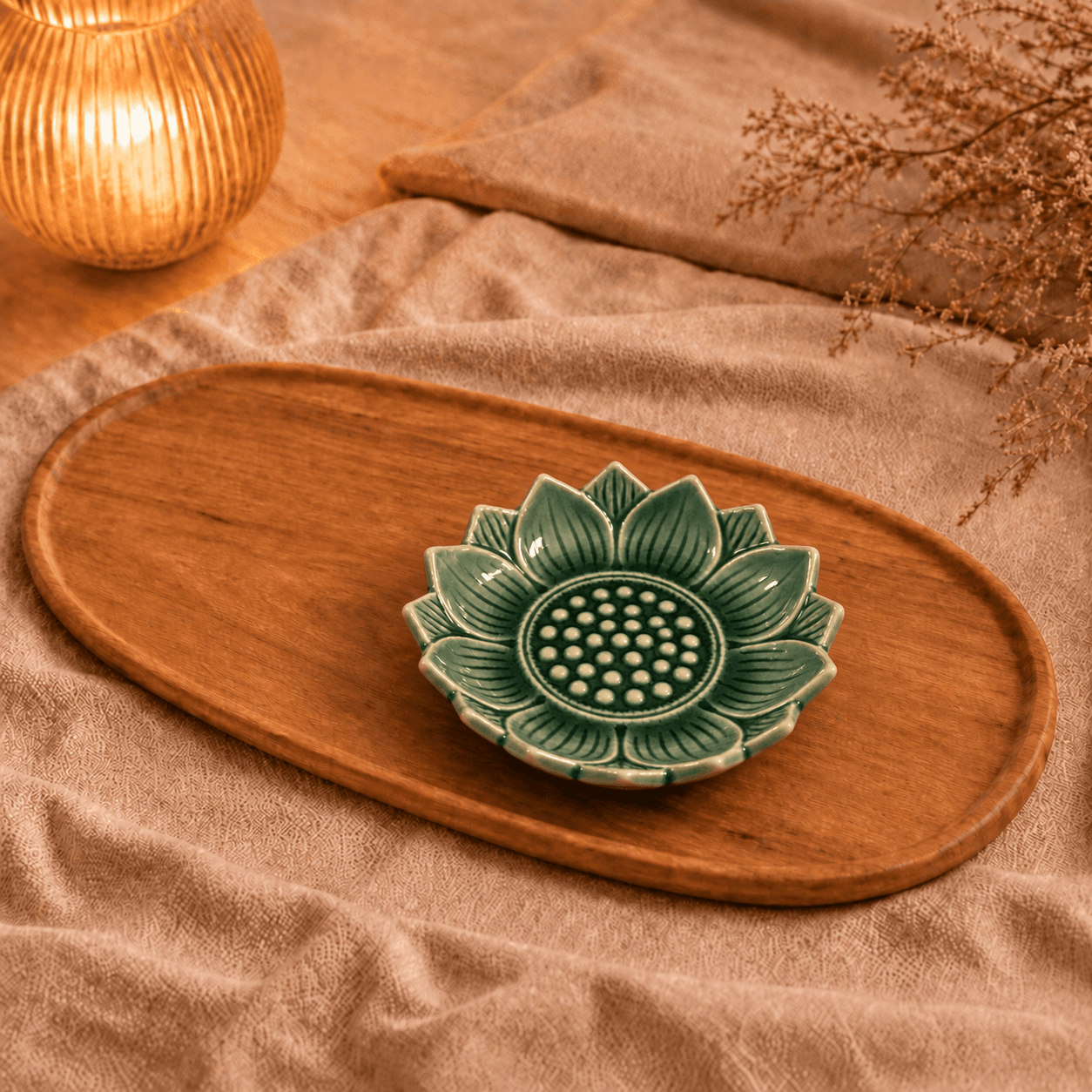 Leeg groen keramieken lotusschaaltje van 9 cm met lotusvormige bloembladeren en reliëf, op een ovaal houten dienblad met beige linnen en warm kaarslicht.