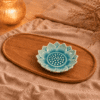 Leeg turquoise keramieken lotusschaaltje van 10 cm met bloemvormig reliëf op een ovaal houten dienblad, sfeervol gestyled met beige linnen en warm kaarslicht.